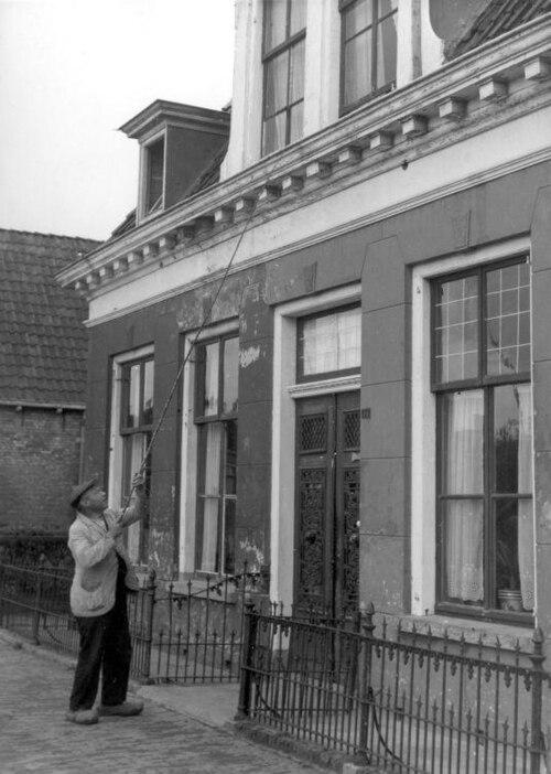A knocker-upper taps an upstairs bedroom window with a long pole